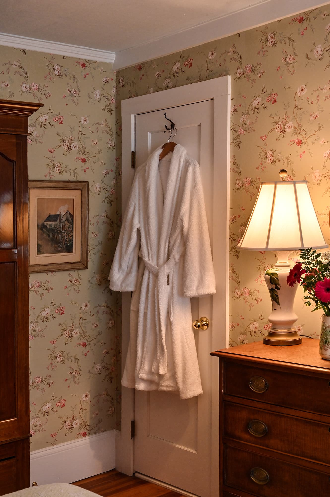 white robes hanging on door by dresser with lamp turned on