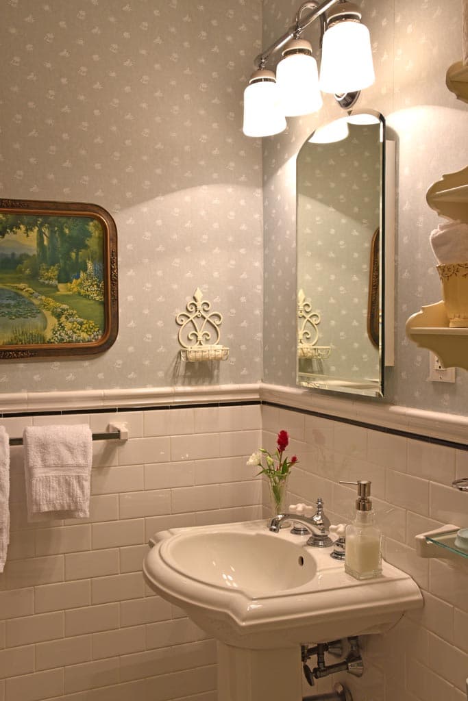 White pedestal sink white subway tile light blue wallpaper vanity lighting over mirror