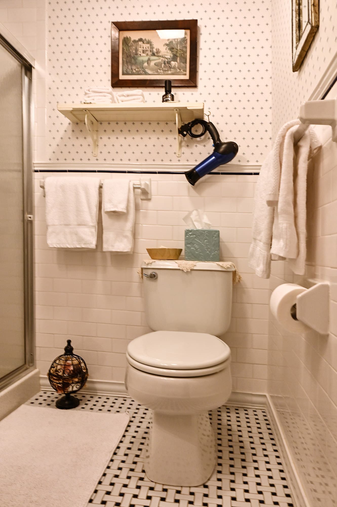 white tiled bath with blue and white wallpaper white towels and shower door