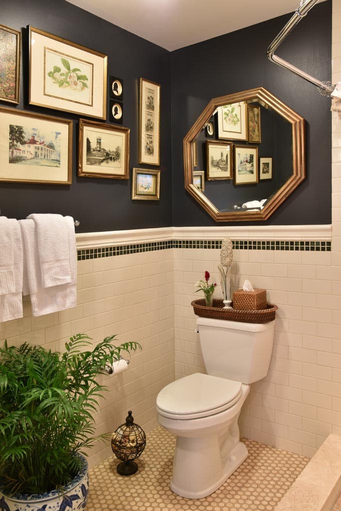 black walls with art gallery above white subway tile white commode with mirror above