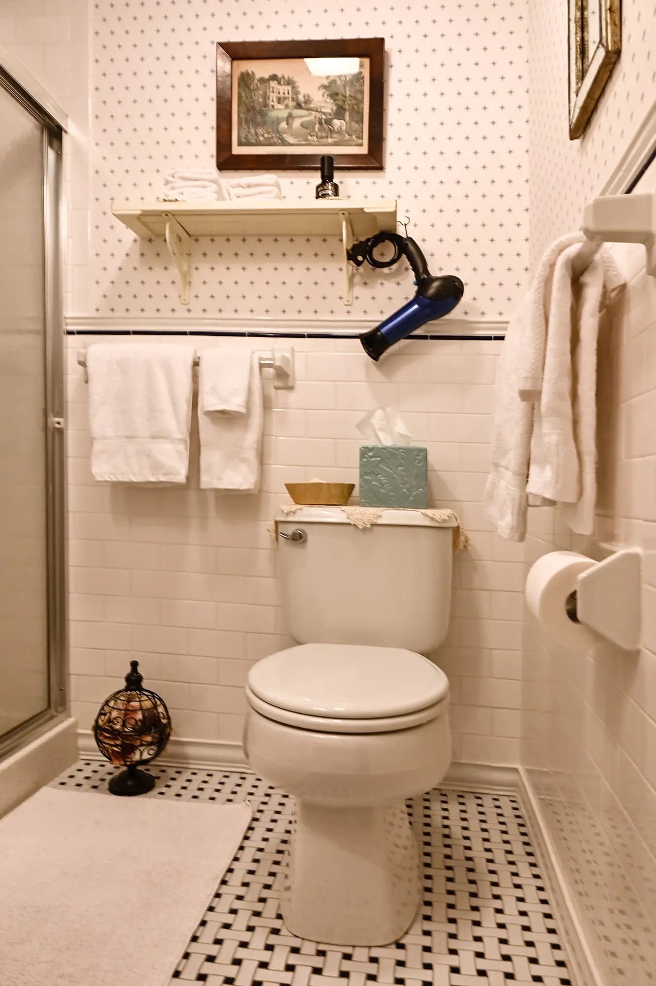 white tiled bath with blue and white wallpaper white towels and shower door