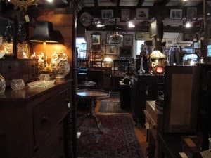 A dimly lit antique shop filled with wooden furniture, decorative glass objects, and vintage lamps.