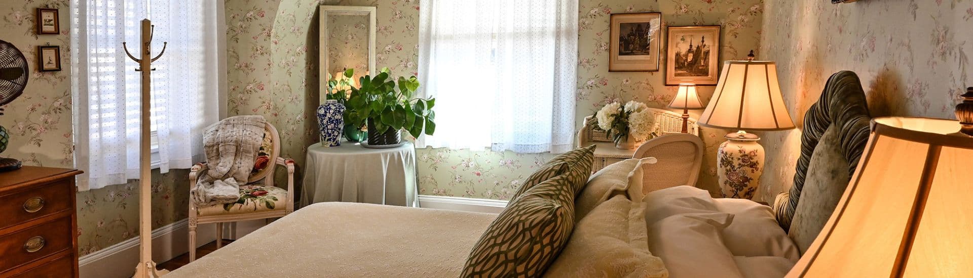 Cozy bedroom with floral wallpaper, soft lighting, and vintage furnishings.