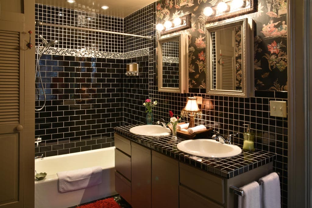 Black tile bathroom. vanity with double white sinks on black tile top mirror above each sink