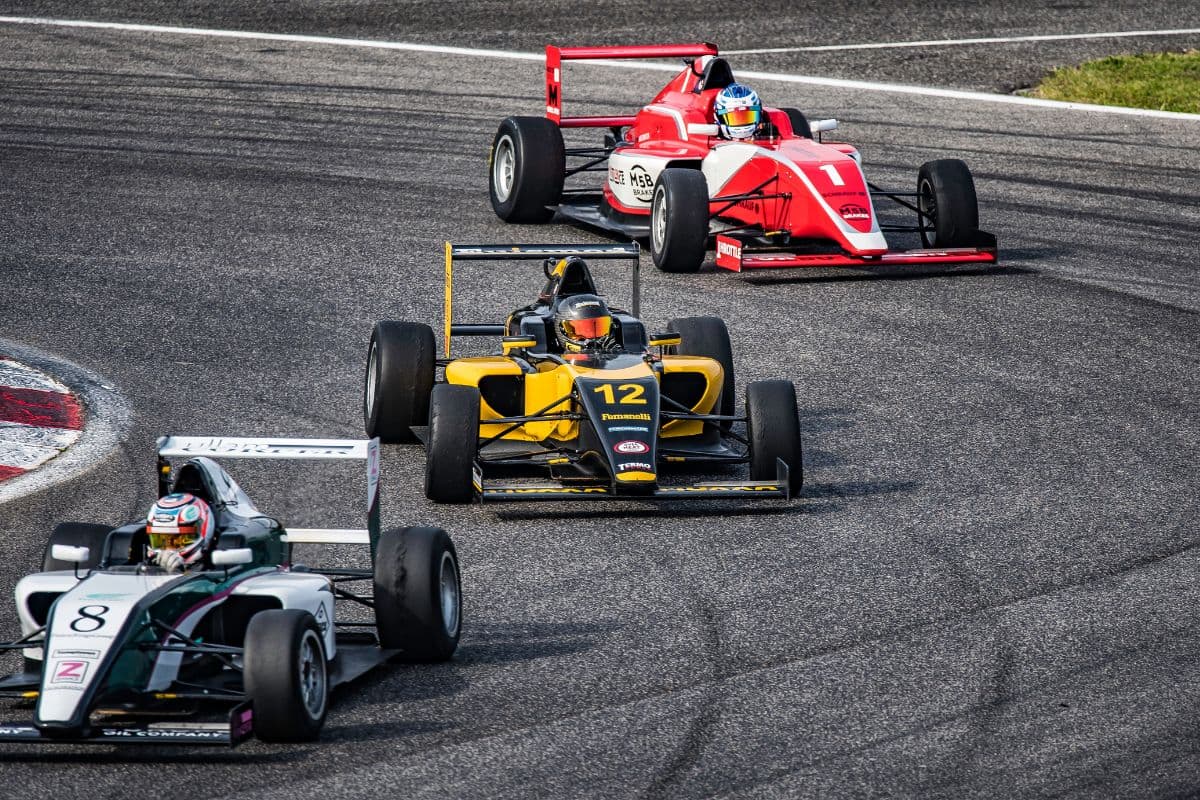 Three race cars navigate a curve on a track during a competition.