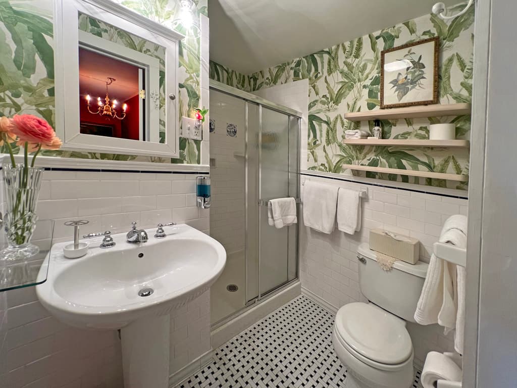 white tiled bath with blue and white wallpaper white towels and shower door