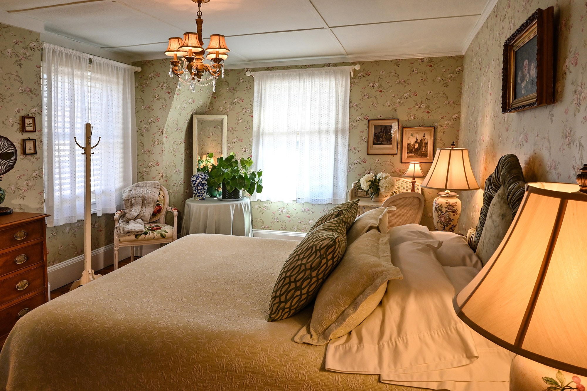 green wallpaper with pink and yellow flowers, bright and sunny two windows, chandelier above bed