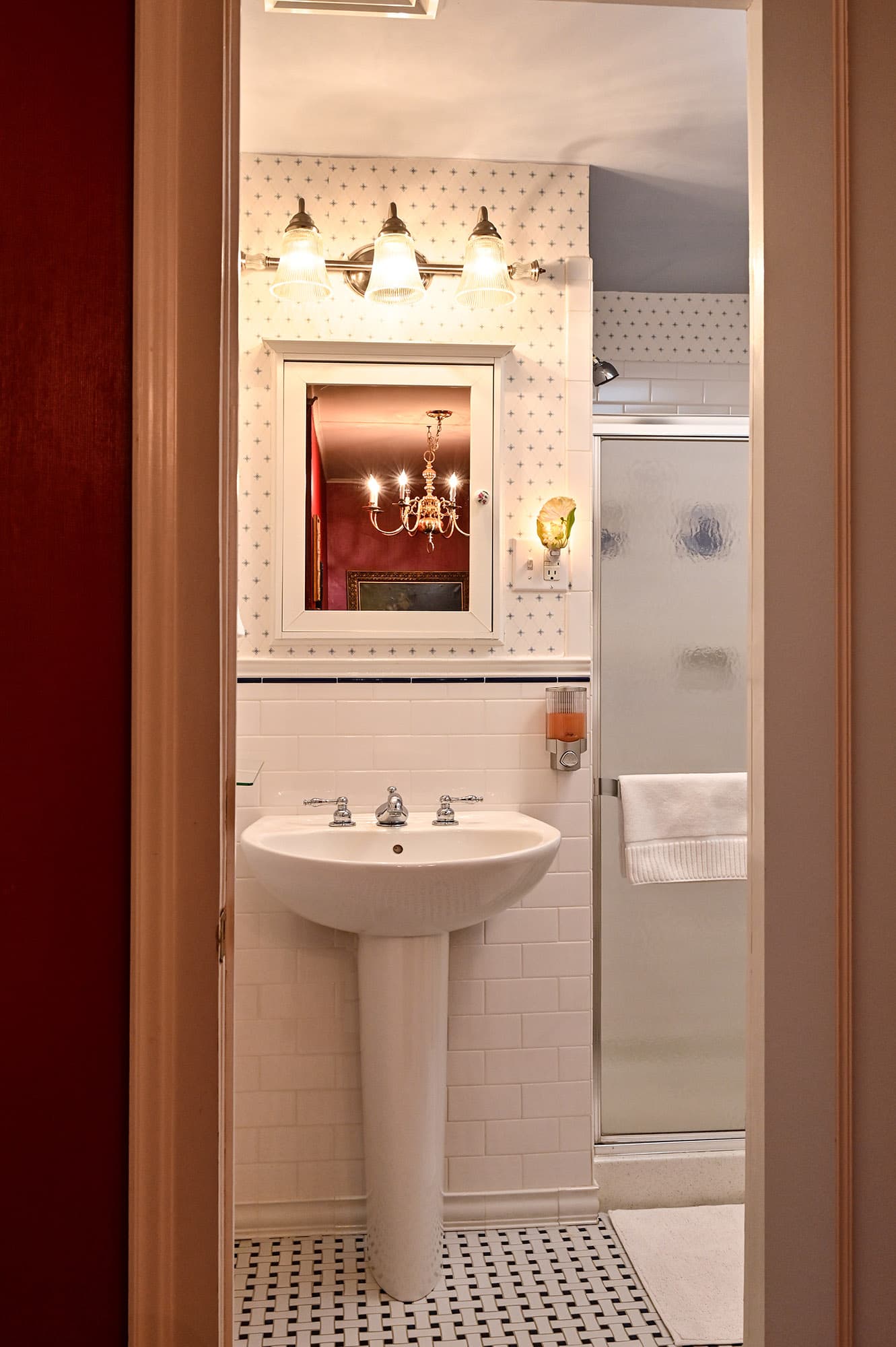 white pedestal sink white subway tile walls and black and white ceramic tile floor. Walk in shower to the right.