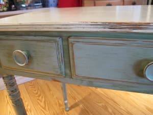 A close-up of a vintage table with a weathered green finish and two wooden drawers.