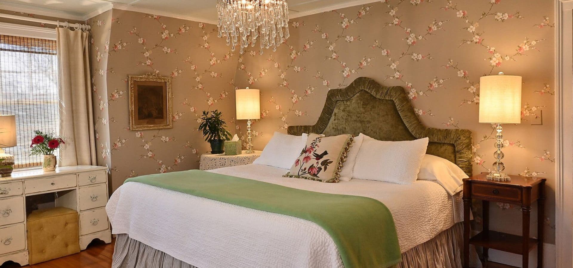 A beautifully decorated bedroom featuring a green-accented bed, floral wallpaper, and elegant lighting.