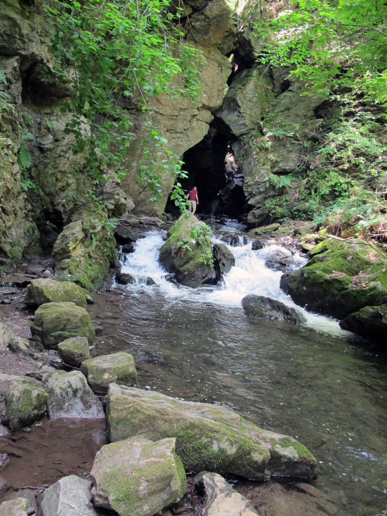 cave with triangle opening and stream running over rocks with people inside cave