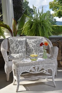 White wicker settee with floral pillow an fern in background