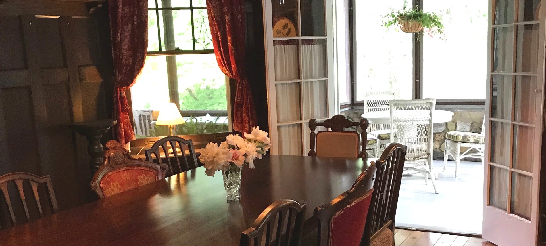 Elegant dining room with large dark brown table, red curtains and French doors opening to a bright patio