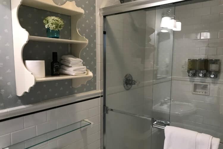 Bathroom with white tile, grey and white wallpaper, and large open shower with glass doors