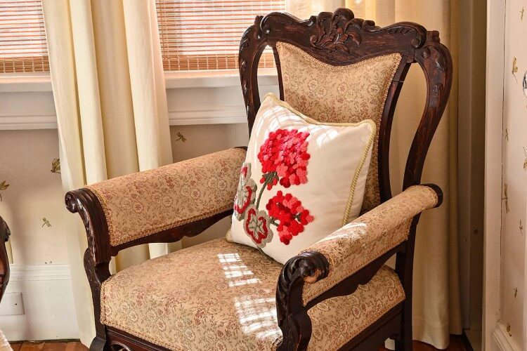 Dark brown wooden sitting chair with pattern cushions and white and red flowered pillow