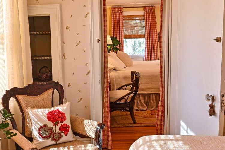 Bedroom with brown sitting chair with doorway looking into another bedroom with queen bed and window