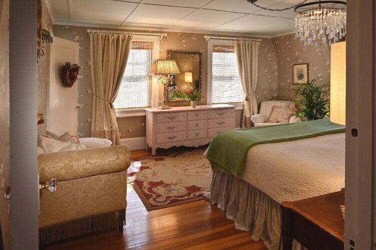 Elegant guest room featuring queen bed, sitting chair, chaise lounger and white dresser