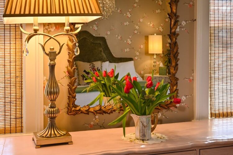 Top of white dresser with ornate mirror, tall silver lamp and small antique pitcher filled with red tulips