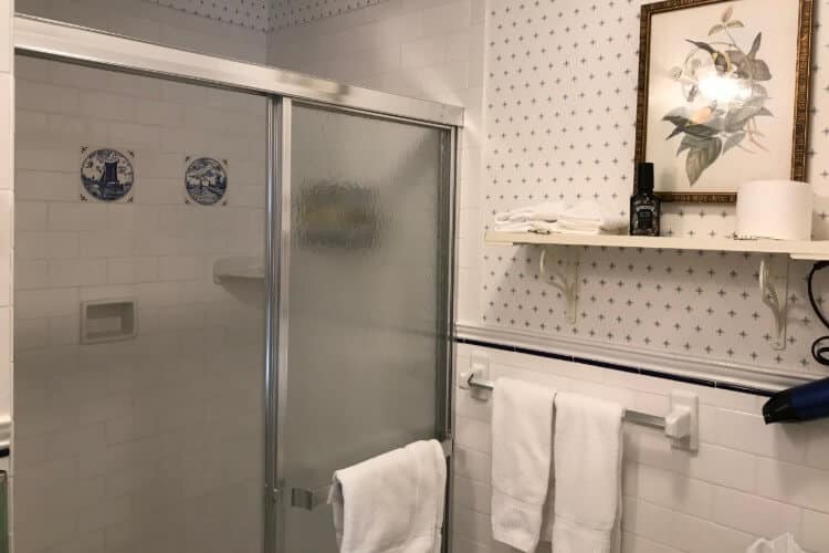 Bathroom with white tile, large open shower with glass doors and blue and white wallpapered walls