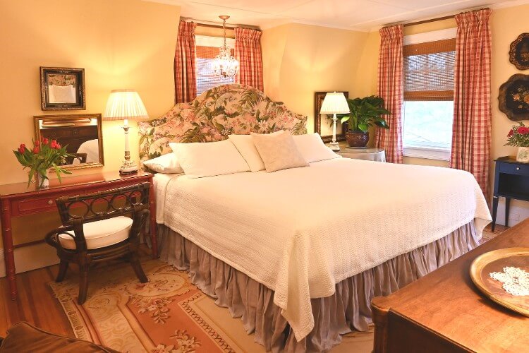 Elegant guest room with king bed, white coverlet, floral headboard and white and red checkered curtains