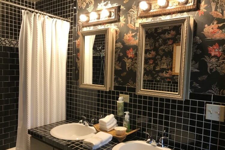 Bathroom with white and black tiled counter and backsplash, two sinks, two mirrors, and white shower curtain