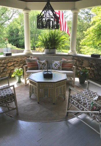 Corner of a stone porch featuring a loveseat, octagon table, two chairs and ornate chandelier on ceiling